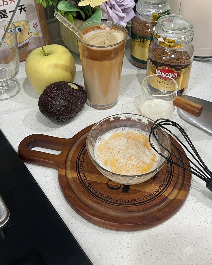 Szklana miska wypełniona ubiotą, spienioną masą z jajka i mleka obok czarnej trzepaczki.