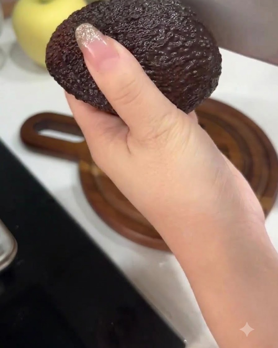 Dłoń trzymająca awokado podczas przekrawania go na pół za pomocą dużego noża kuchennego.