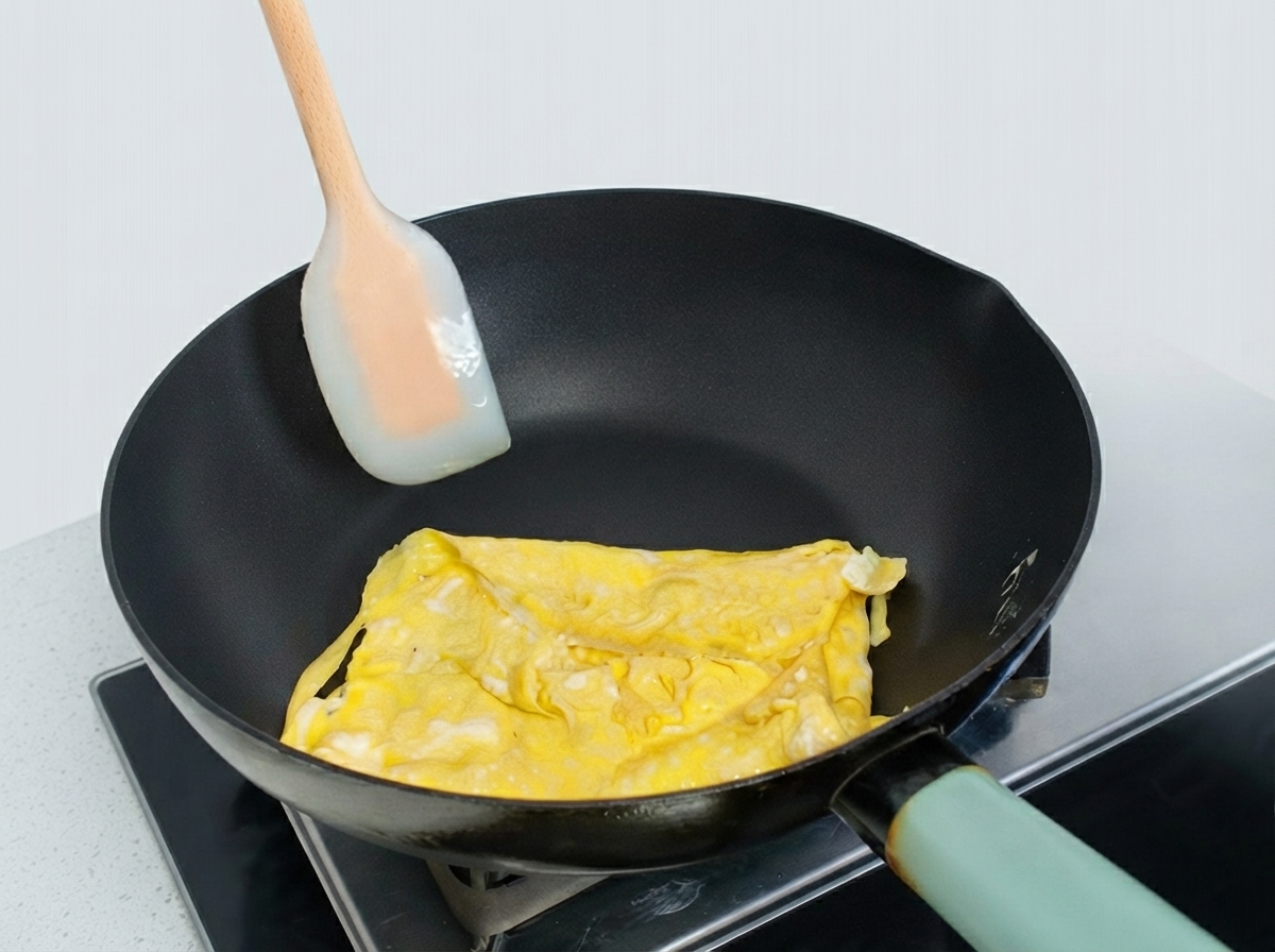 Częściowo złożony omlet jajeczny na patelni formowany za pomocą silikonowej łopatki.