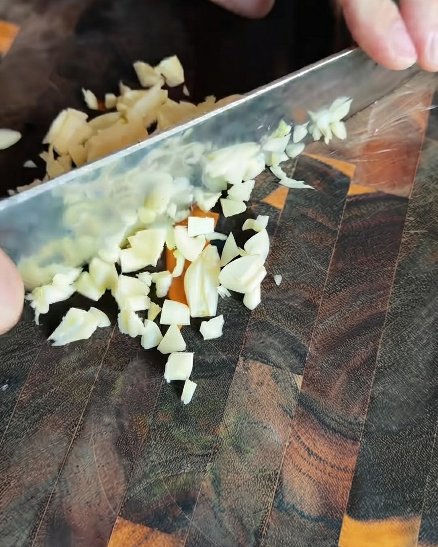 Świeżo posiekane kawałki czosnku rozsypane na ciemnej drewnianej desce do krojenia.