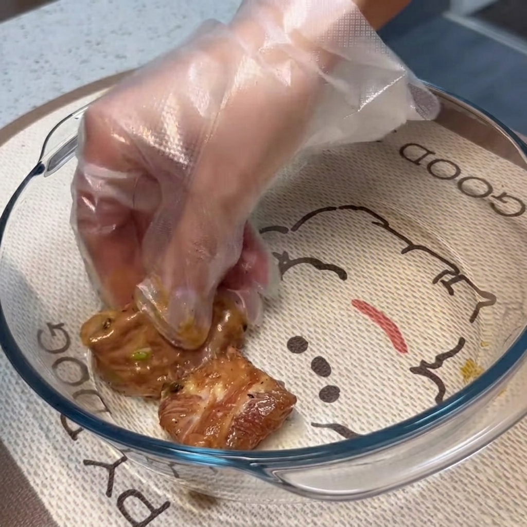 Zamarynowane żeberka wieprzowe ułożone płasko w jednej warstwie w przezroczystym szklanym naczyniu do pieczenia.