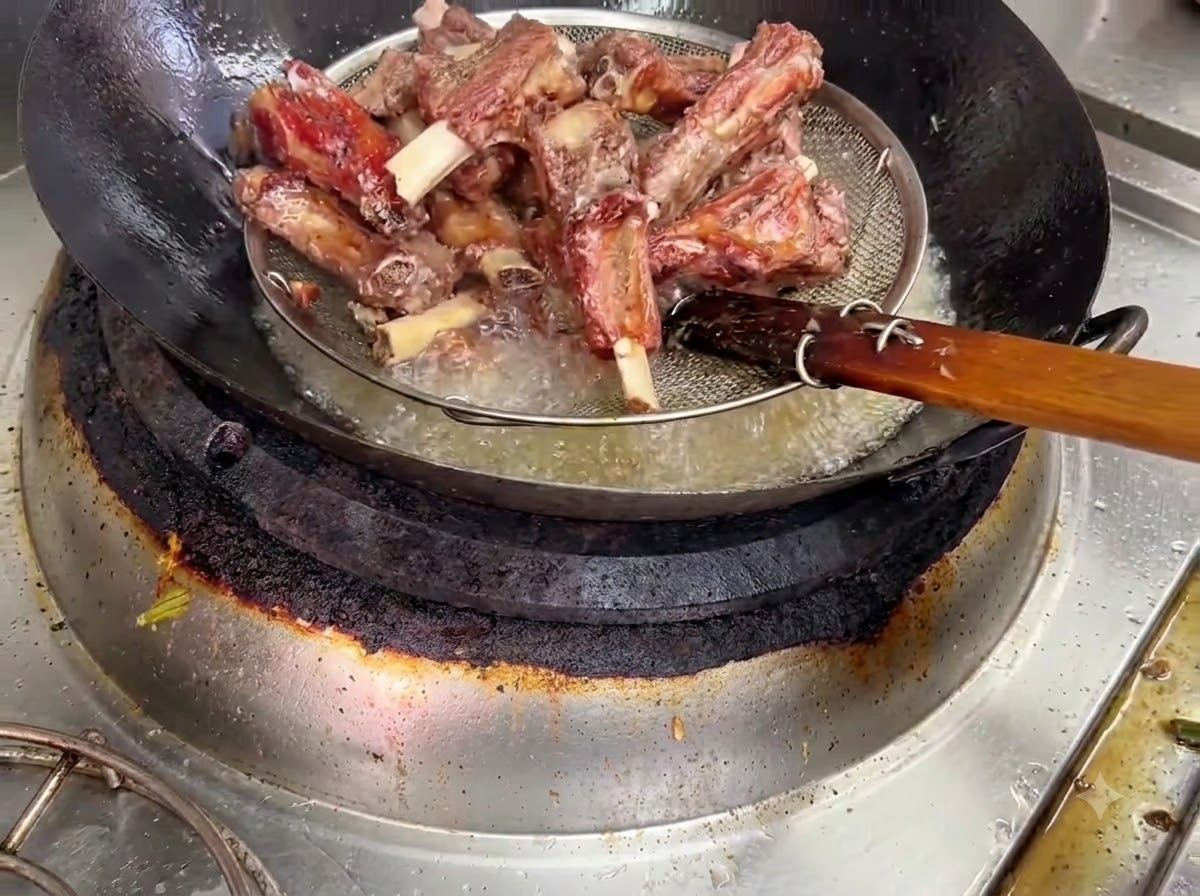 Usmażone żeberka wieprzowe wyciągane z gorącego oleju za pomocą koszyka z siatki drucianej.