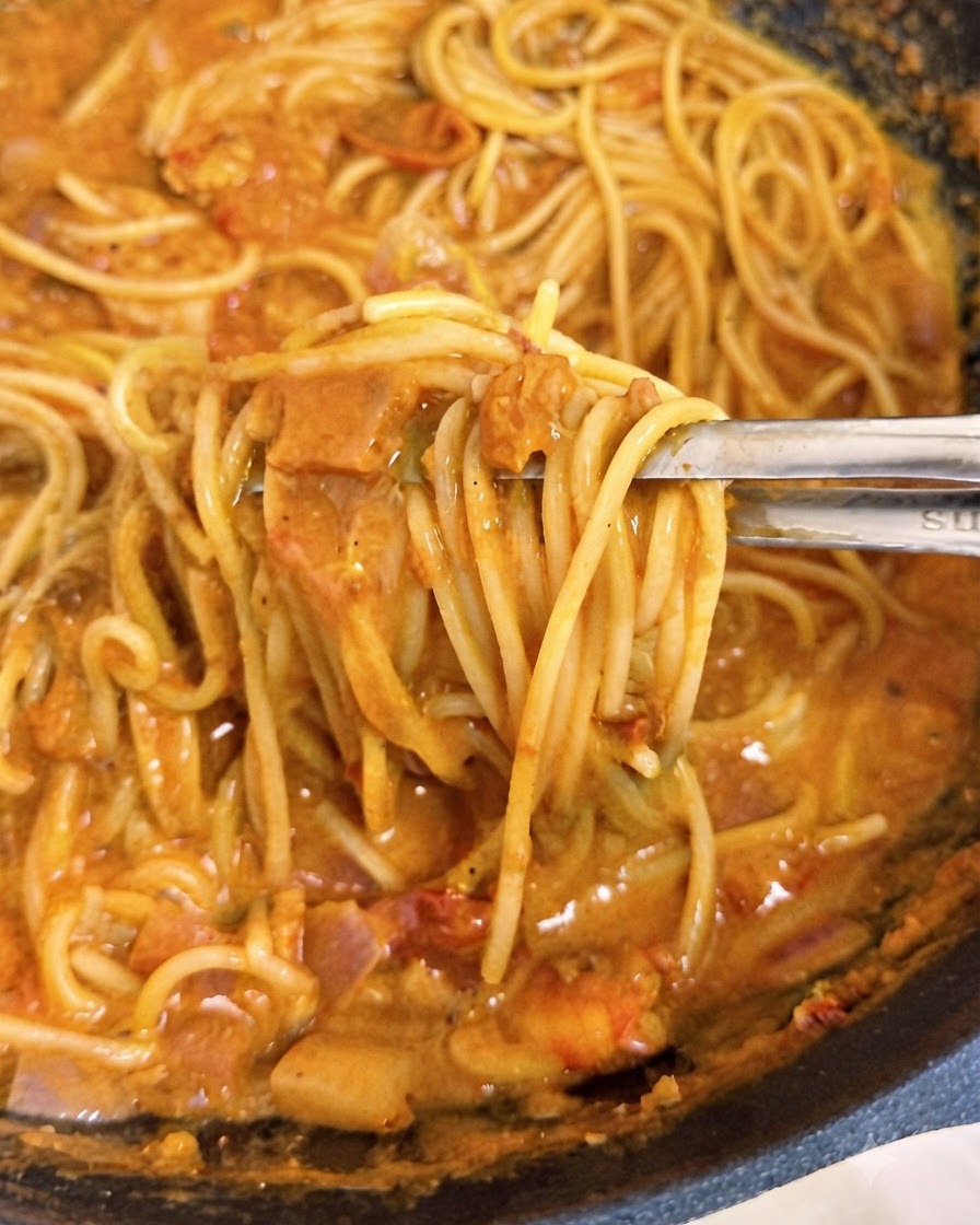 Szczypce unoszące nitki spaghetti otoczone kremowym, różowym sosem pomidorowym wewnątrz woka.