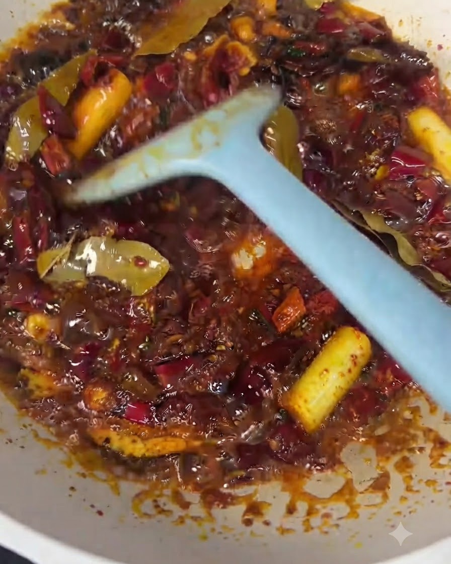 Kawałki wołowiny mieszane z czerwonym olejem chili i bazą przypraw za pomocą niebieskiej łopatki.
