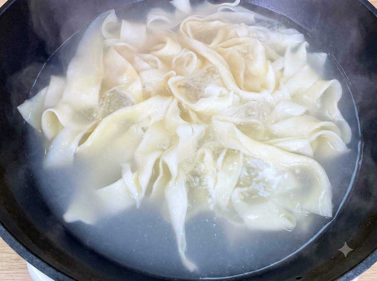 Świeża kapusta bok choy gotująca się razem z szerokim makaronem na patelni.