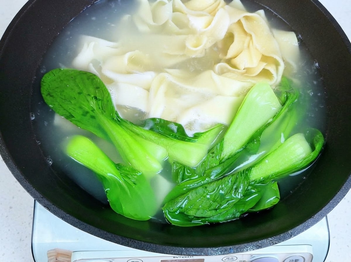 Pałeczki wyjmujące ugotowany szeroki makaron i bok choy z gorącej wody.