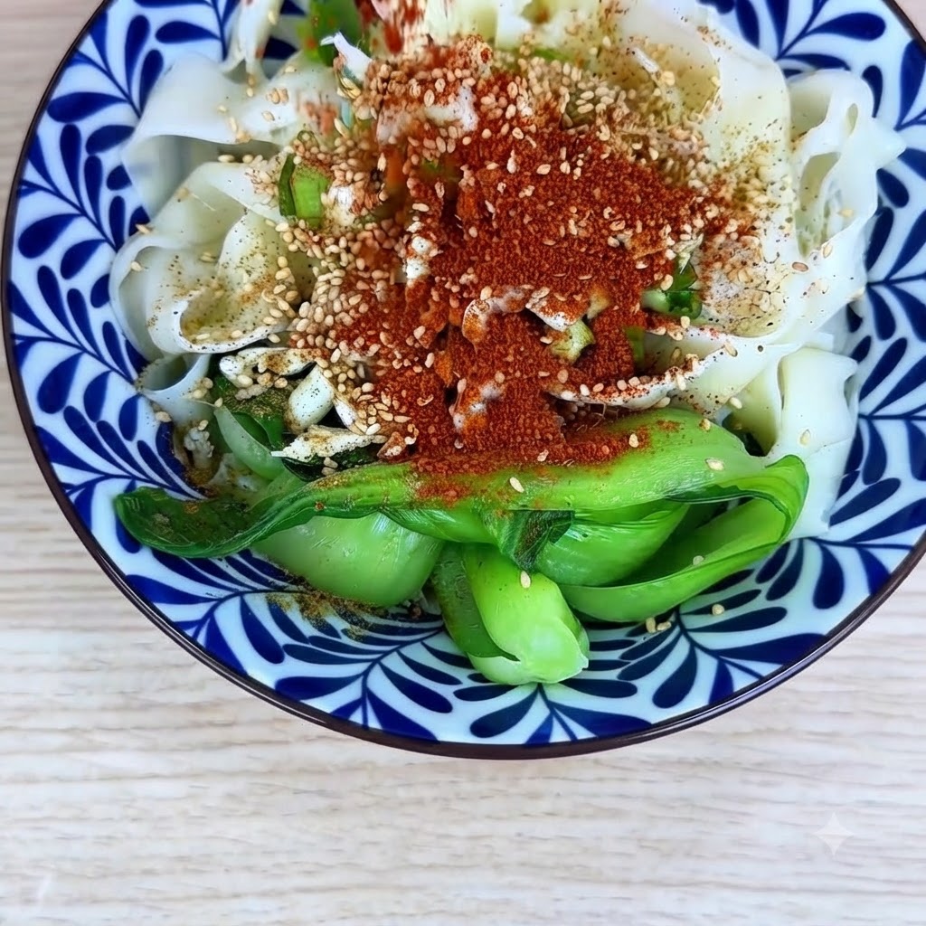 Drobne chili w proszku i grubo mielone chili rozsypane równomiernie na wierzchu makaronu i dodatków w misce.