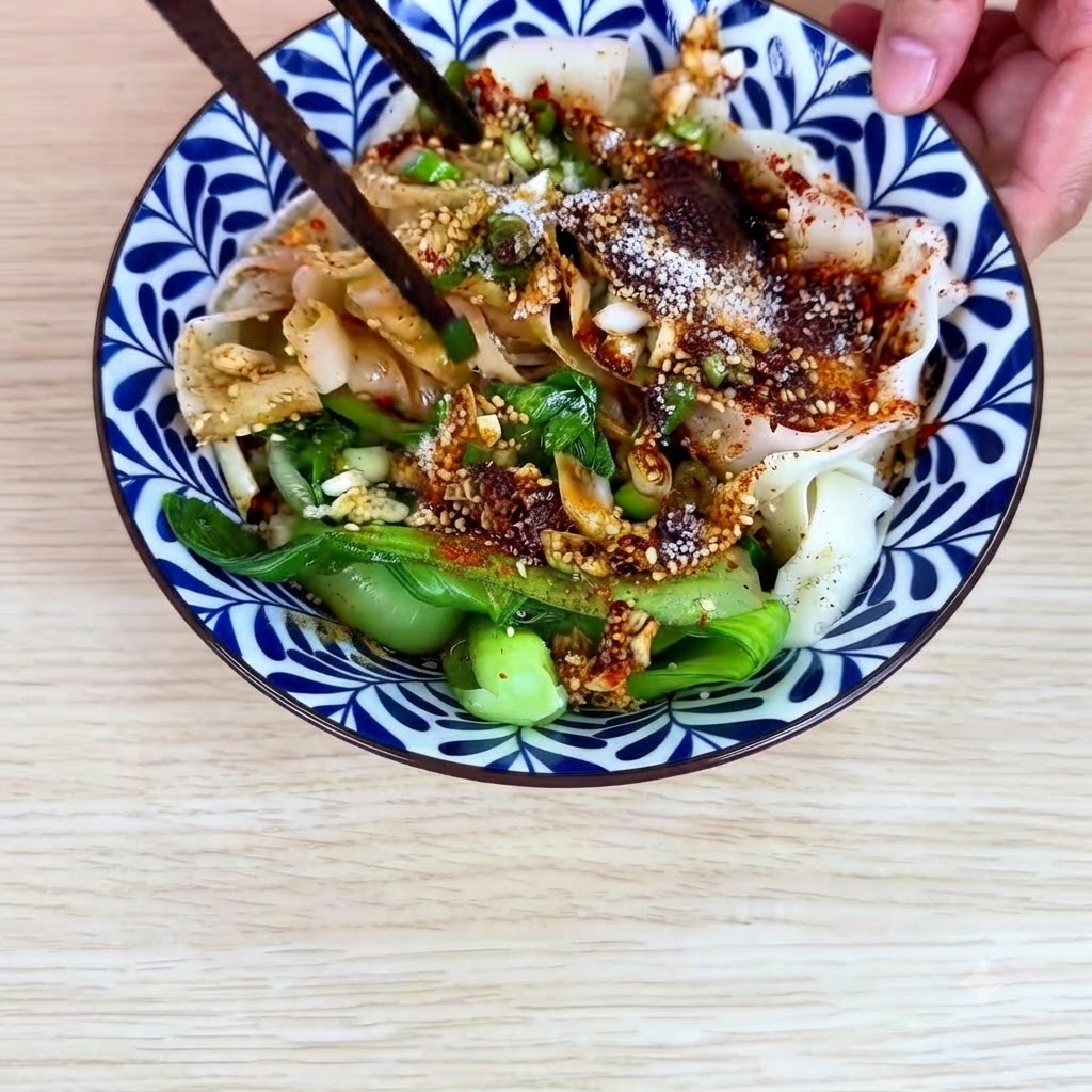 Pałeczki mieszające szeroki makaron pszenny, bok choy i sos z chili razem w ceramicznej misce.