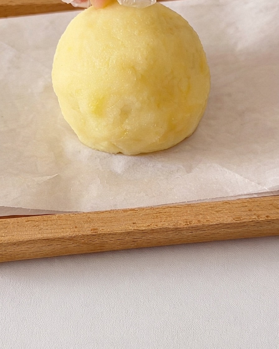 Okrągła kula gładkiego purée ziemniaczanego formowana dłońmi z małymi kawałkami ziemniaków dodanymi na górę w celu utworzenia uszu.