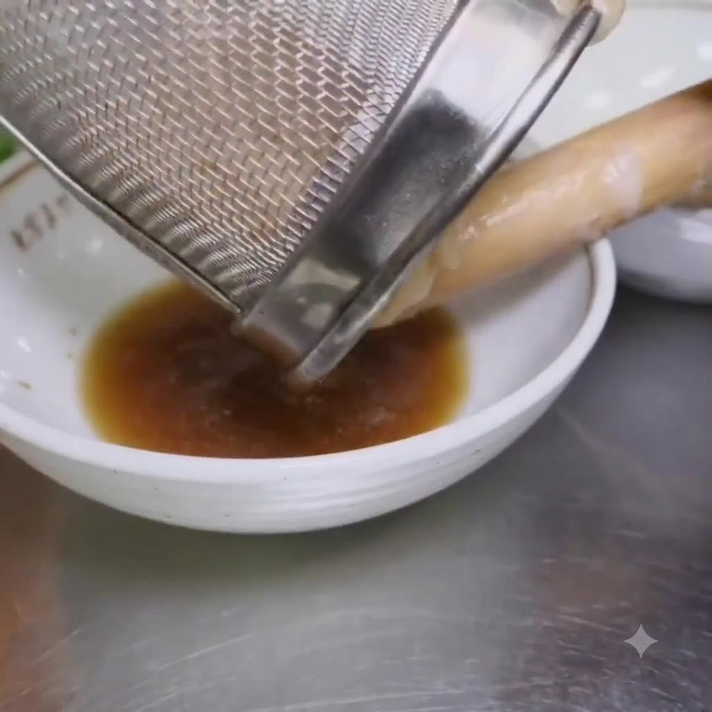 Ugotowany makaron ramen przekładany z sitka siatkowego do miski zawierającej przyprawę.
