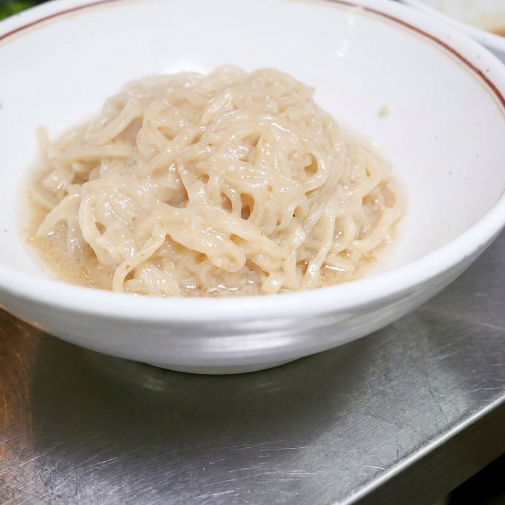 Ugotowany makaron ramen leżący schludnie w białej misce, gotowy do wymieszania z sosem.
