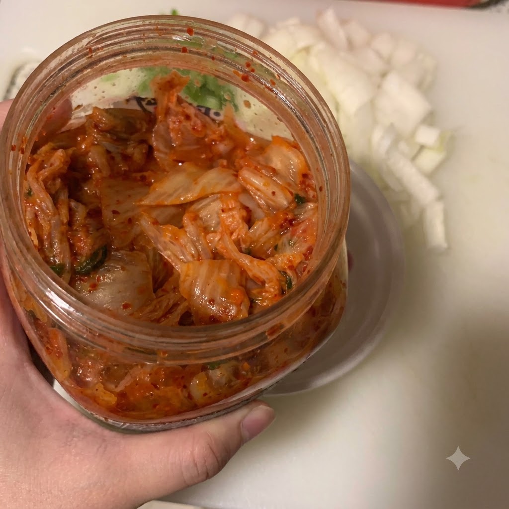 Kimchi nakładane łyżką do małej białej miski obok pojemnika z posiekaną cebulą.