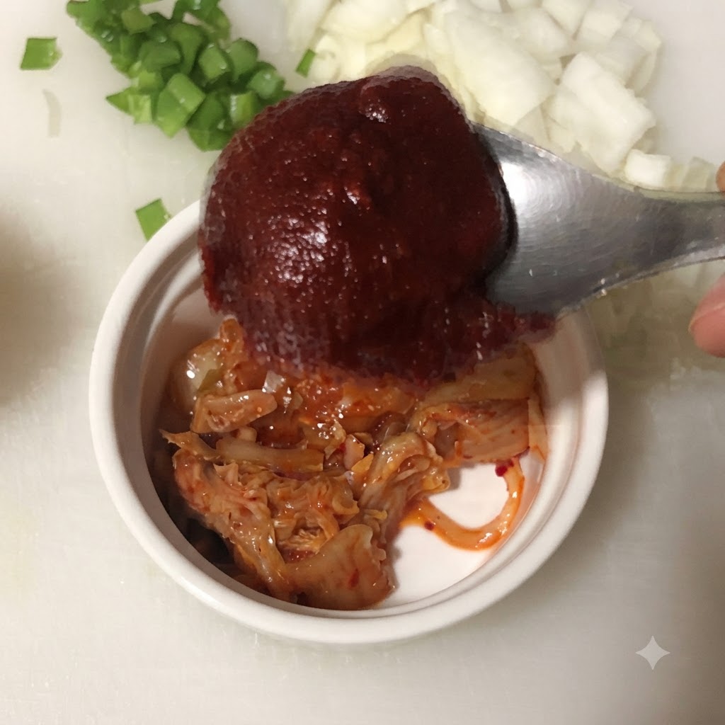 Łyżka koreańskiej pasty chili trzymana nad miską zawierającą posiekane kimchi.