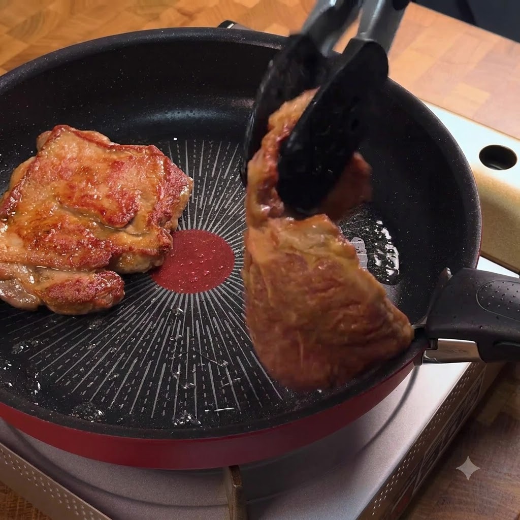 Szczypce kuchenne przewracające złocisty kotlet schabowy na patelni.