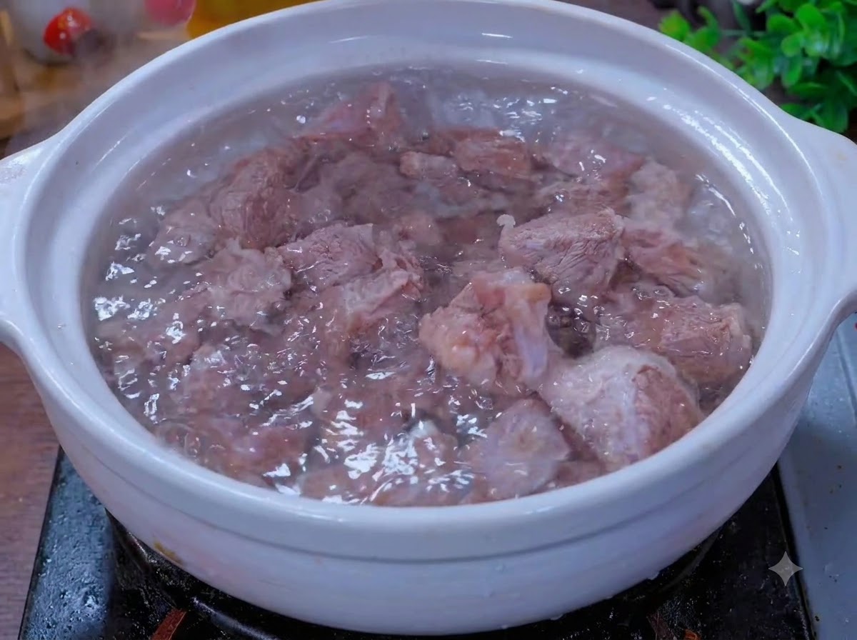 Kawałki wołowiny gotujące się na wolnym ogniu w białym glinianym garnku z aromatycznymi dodatkami.
