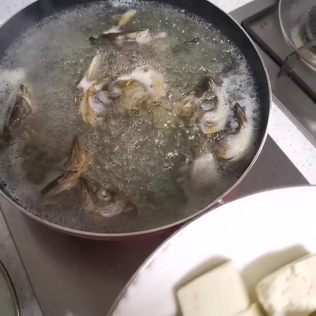 Kostki tofu dodawane do bulgoczącego garnka z zupą z głów ryb.