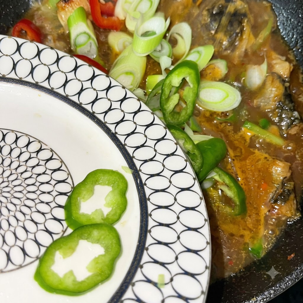 Świeżo pokrojona zielona cebulka oraz czerwona i zielona papryczka chili wsypywane z białego talerza do gotującego się garnka.