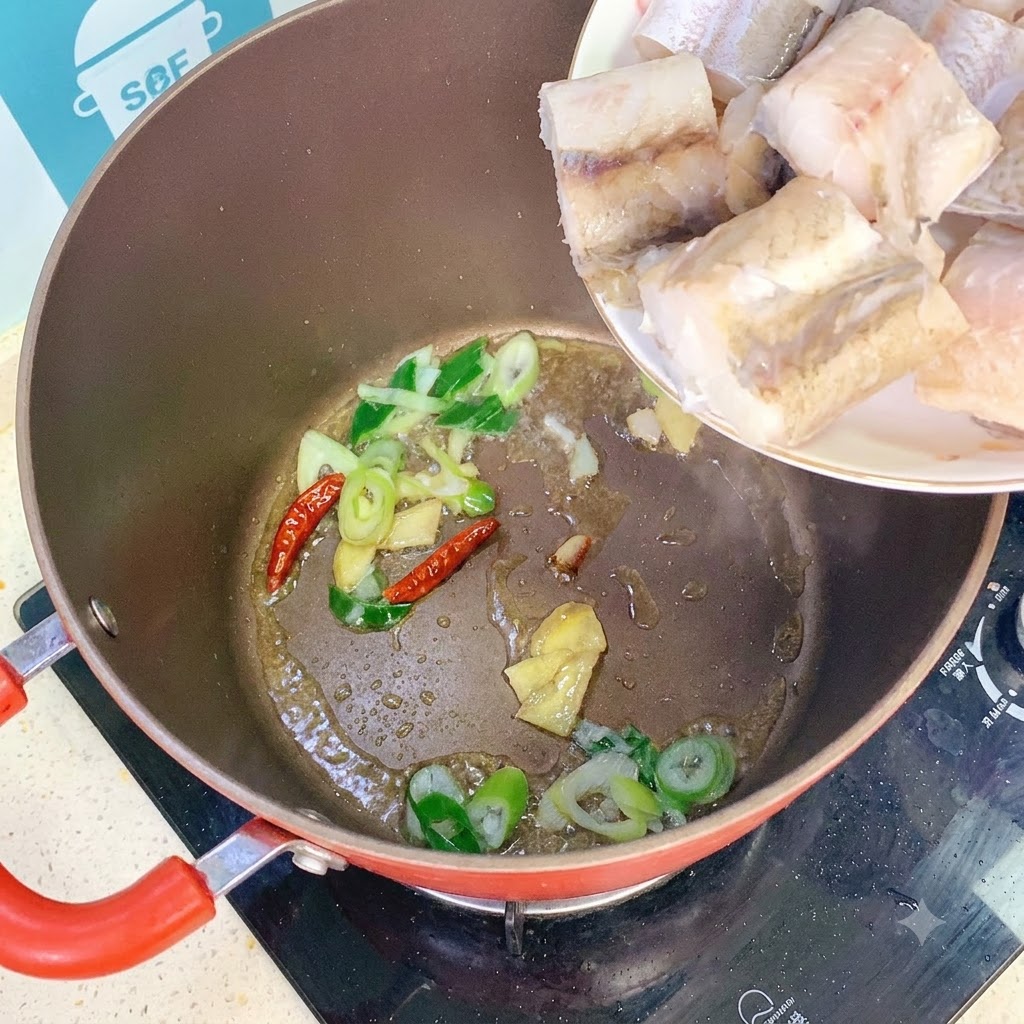 Kawałki mintaja dodawane z talerza do garnka z podsmażoną dymką, imbirem i papryczkami chili.