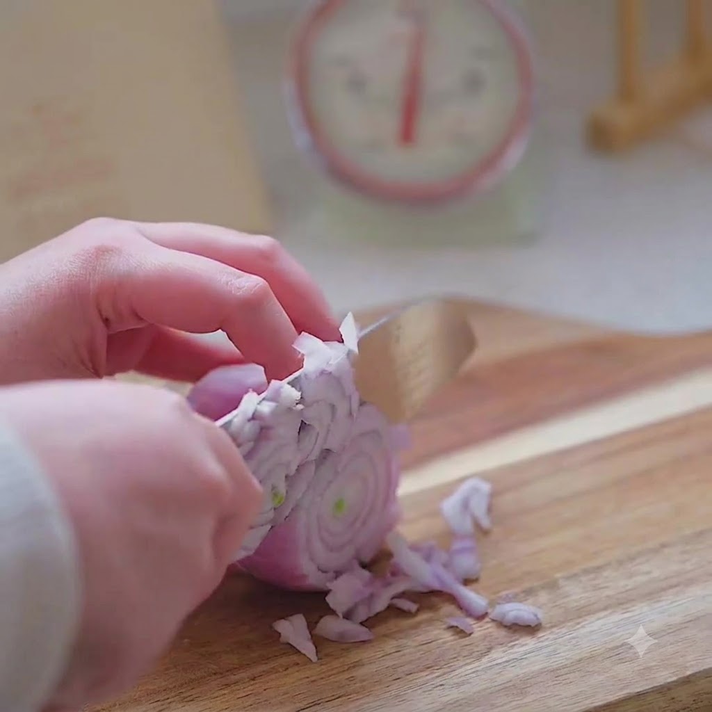 Dłoń trzymająca nóż kuchenny, starannie krojąca czerwoną cebulę w drobną kostkę na drewnianej desce.
