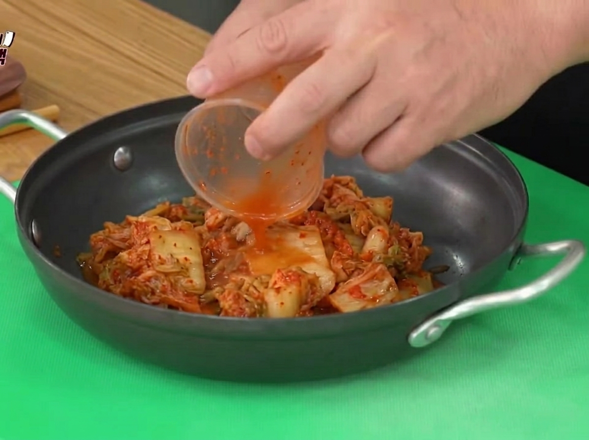 Kwaśne kimchi przekładane z plastikowego pojemnika do czarnego garnka do gotowania.