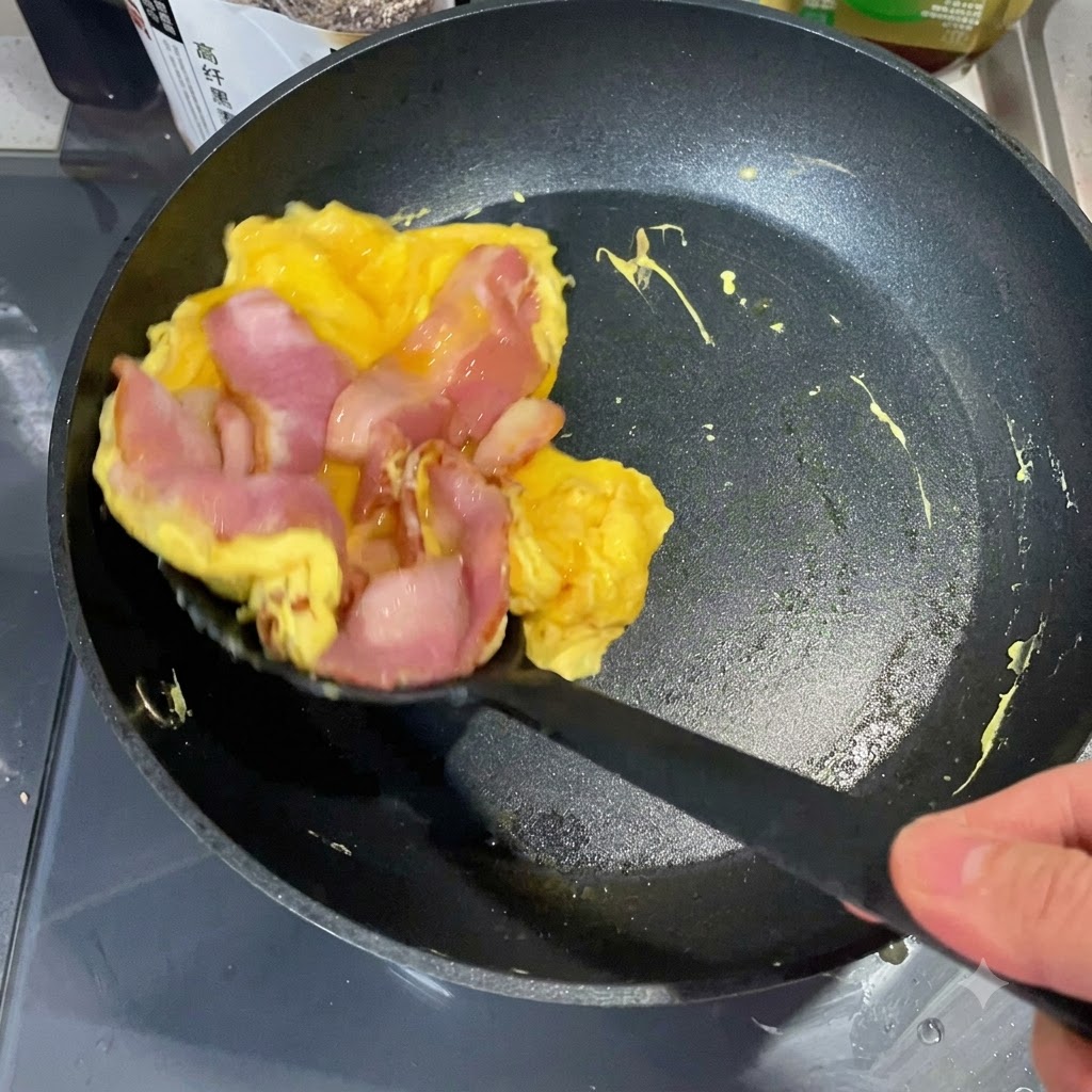 Łopatka kuchenna podnosząca usmażoną warstwę jajka i boczku z patelni, aby położyć ją na połówce z tostowanego muffina angielskiego.