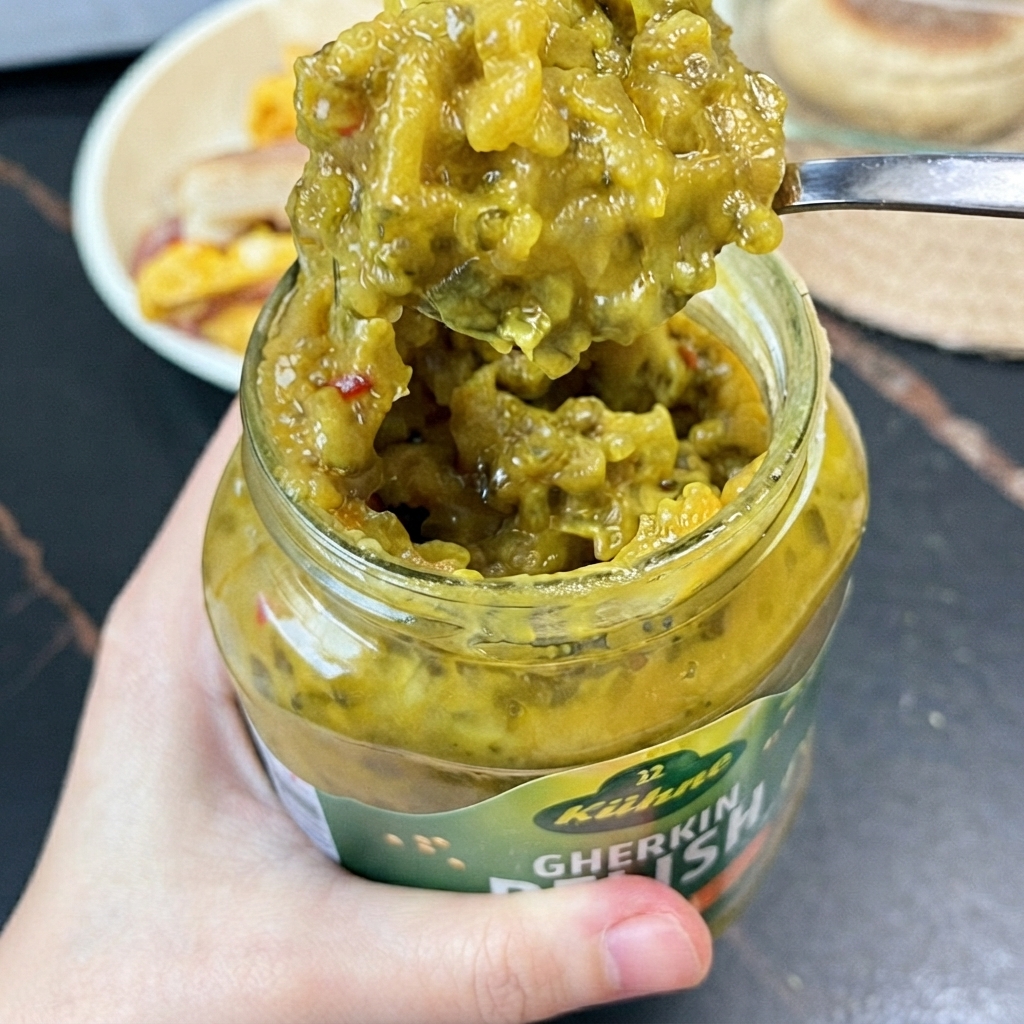 Łyżeczka jasny zielony relish z korniszonów nabierana z szklanego słoika małą łyżeczką.