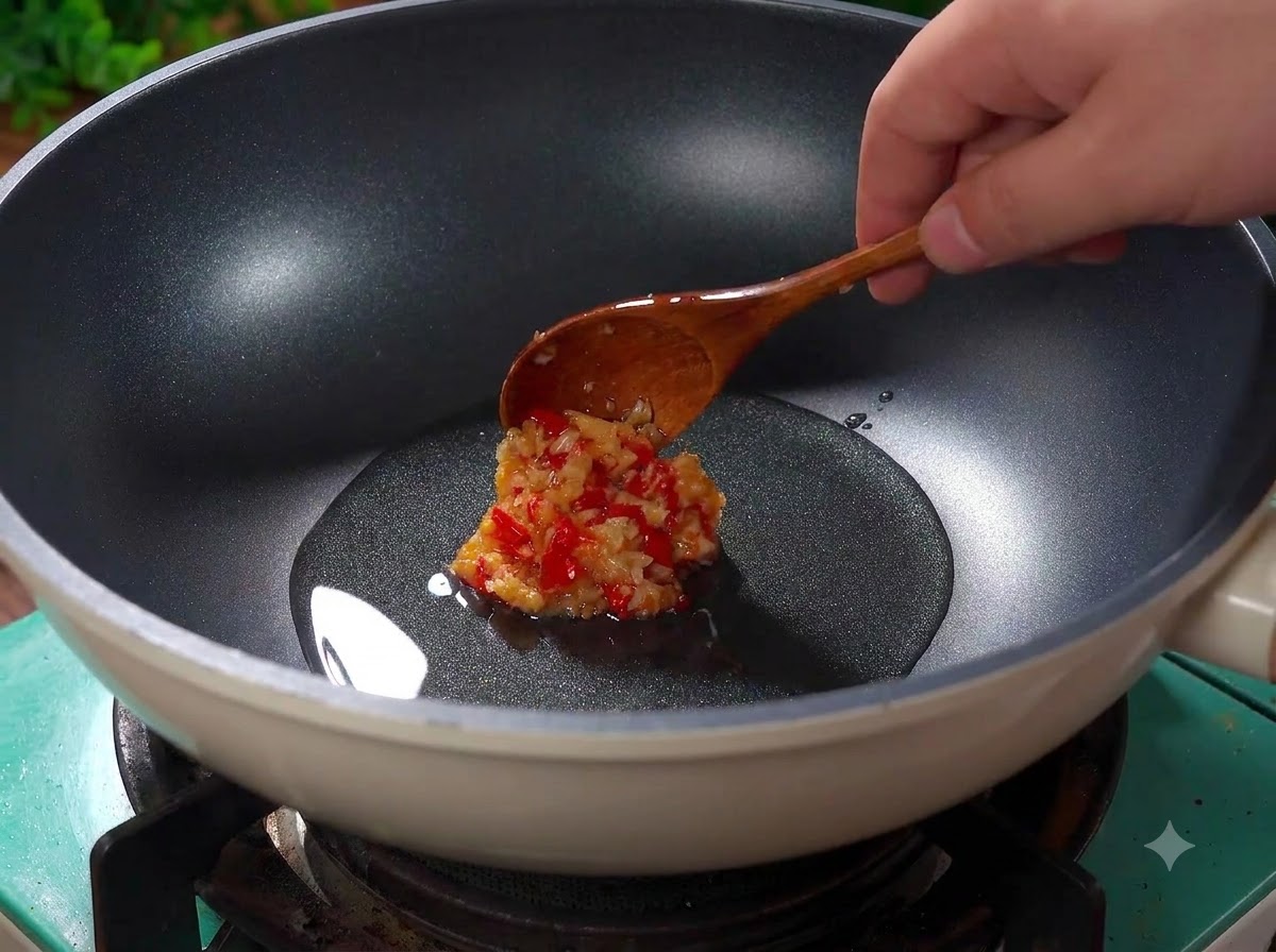 Posiekany czosnek i posiekane czerwone chili skwierczące w gorącym oleju w woku.