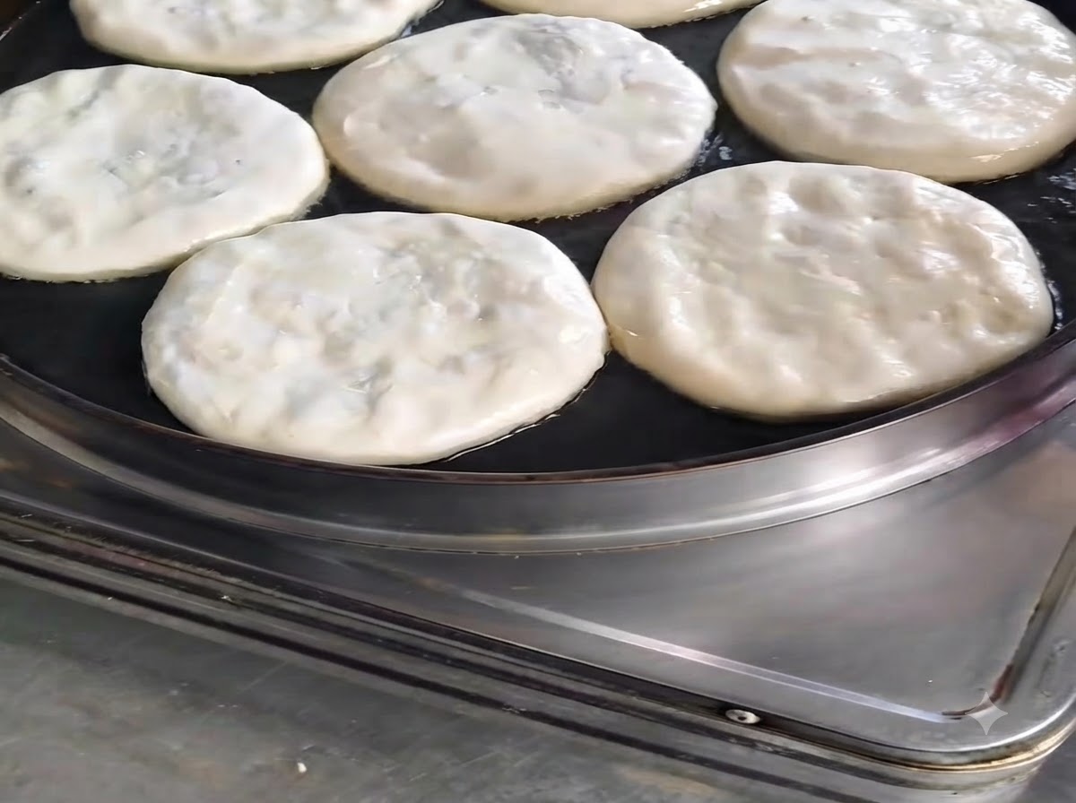 Kilka okrągłych pierogów mięsnych smażących się na patelni z olejem skropionym od góry.