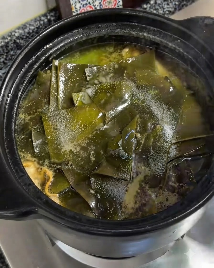 Drobną sól posypana bezpośrednio na kawałki zielonych wodorostów kelp pływające w gotującym się glinianym garnku.