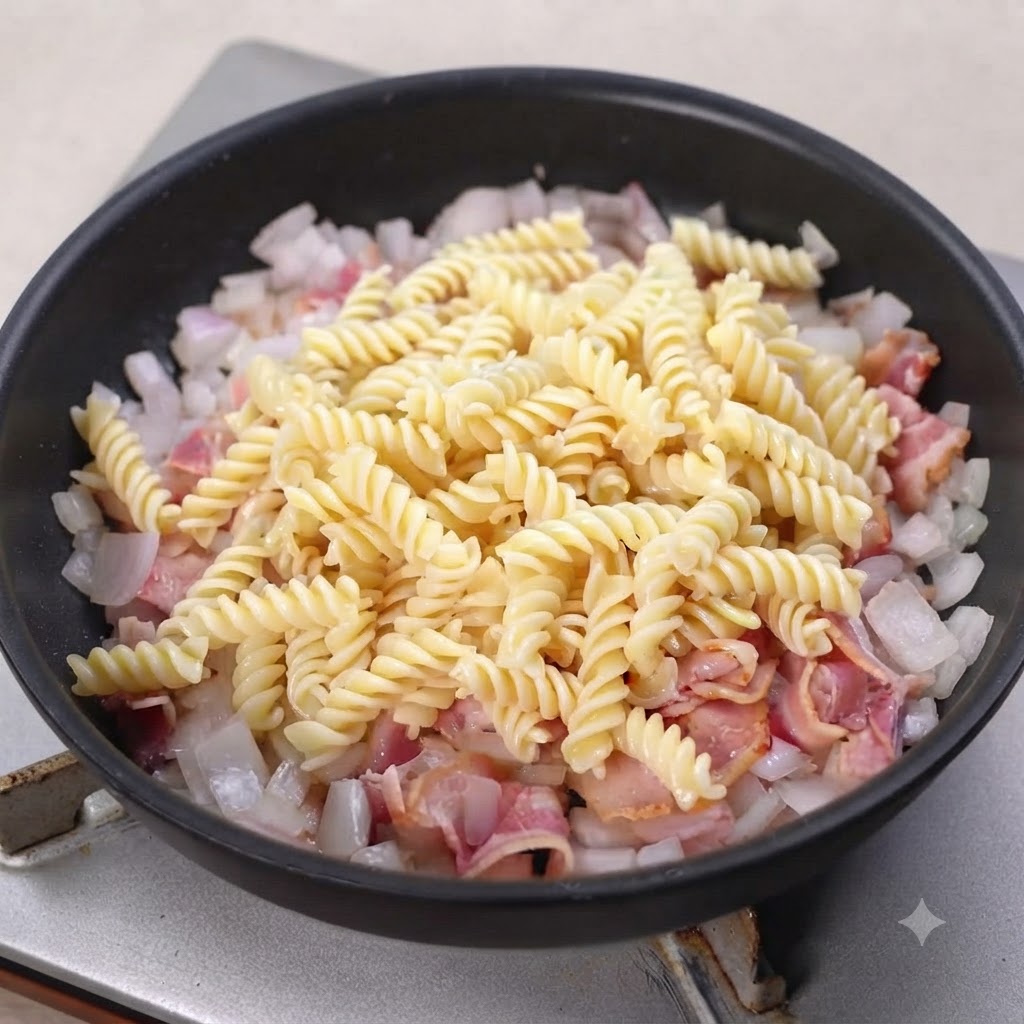 Ugotowany makaron fusilli dodany do chrupiącego boczku i cebuli na patelni.