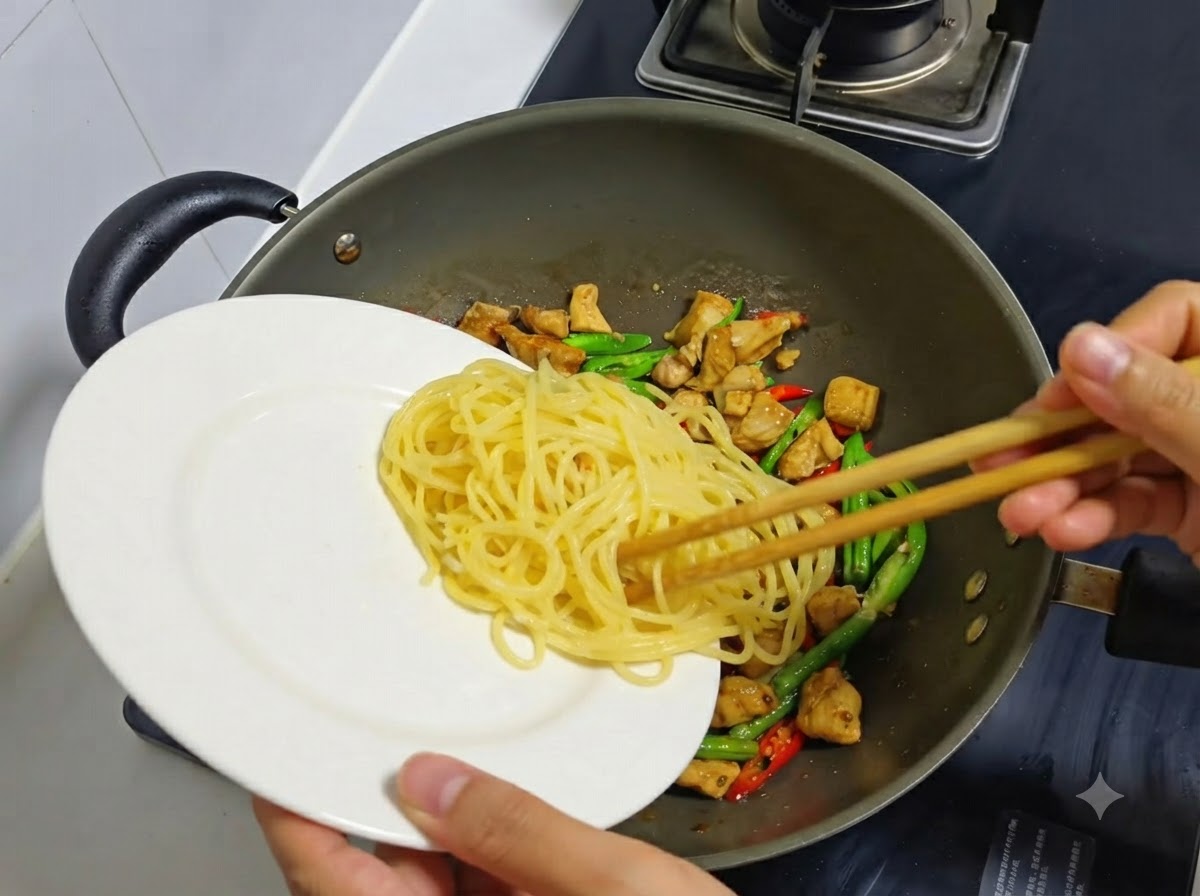 Ugotowany i wystudzony makaron spaghetti przekładany z białego talerza do woka zawierającego kurczaka i chili.