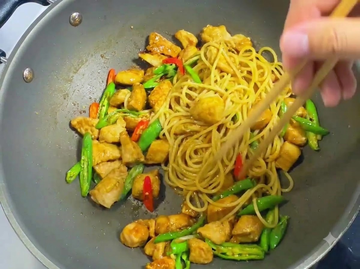 Drewniane pałeczki mieszające i obracające makaron spaghetti, pokrojonego kurczaka, plasterki chili i ciemny sos w woku.