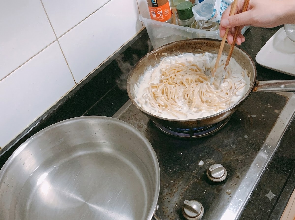 Makaron mieszany z bulgoczącym sosem śmietankowym na patelni za pomocą pałeczek.