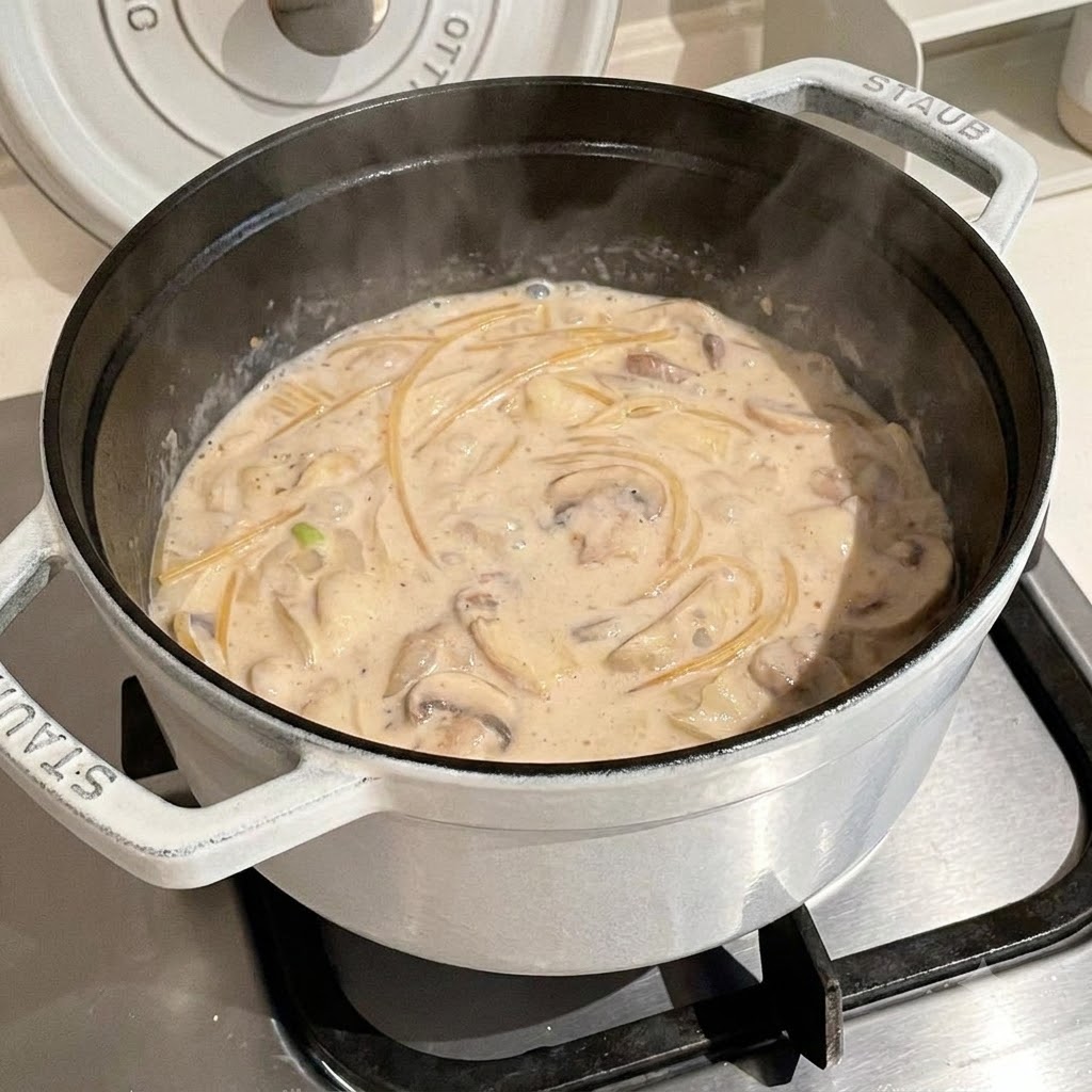 Makaron spaghetti gotujący się w bulgoczącym, kremowym bulionie w białym garnku.