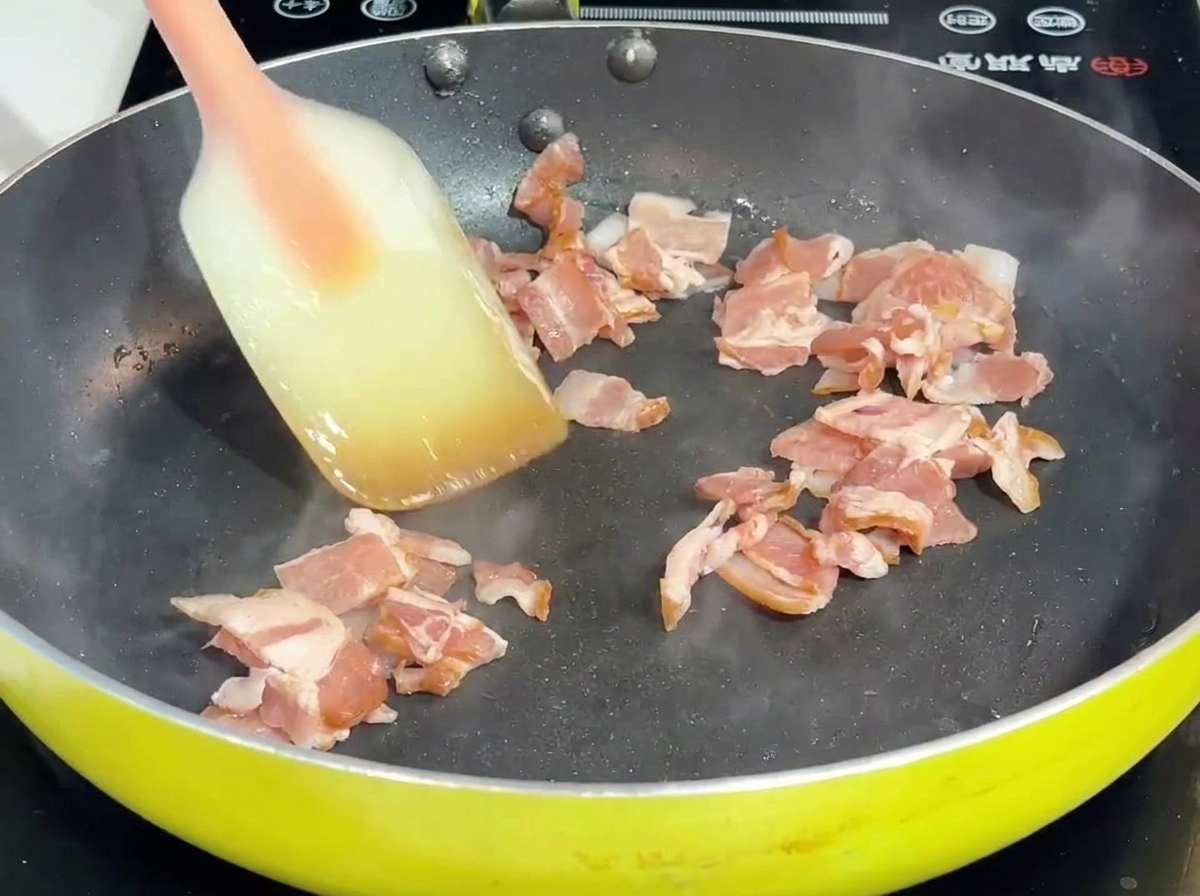 Boczek i cebula smażone na patelni przy użyciu szpatułki.