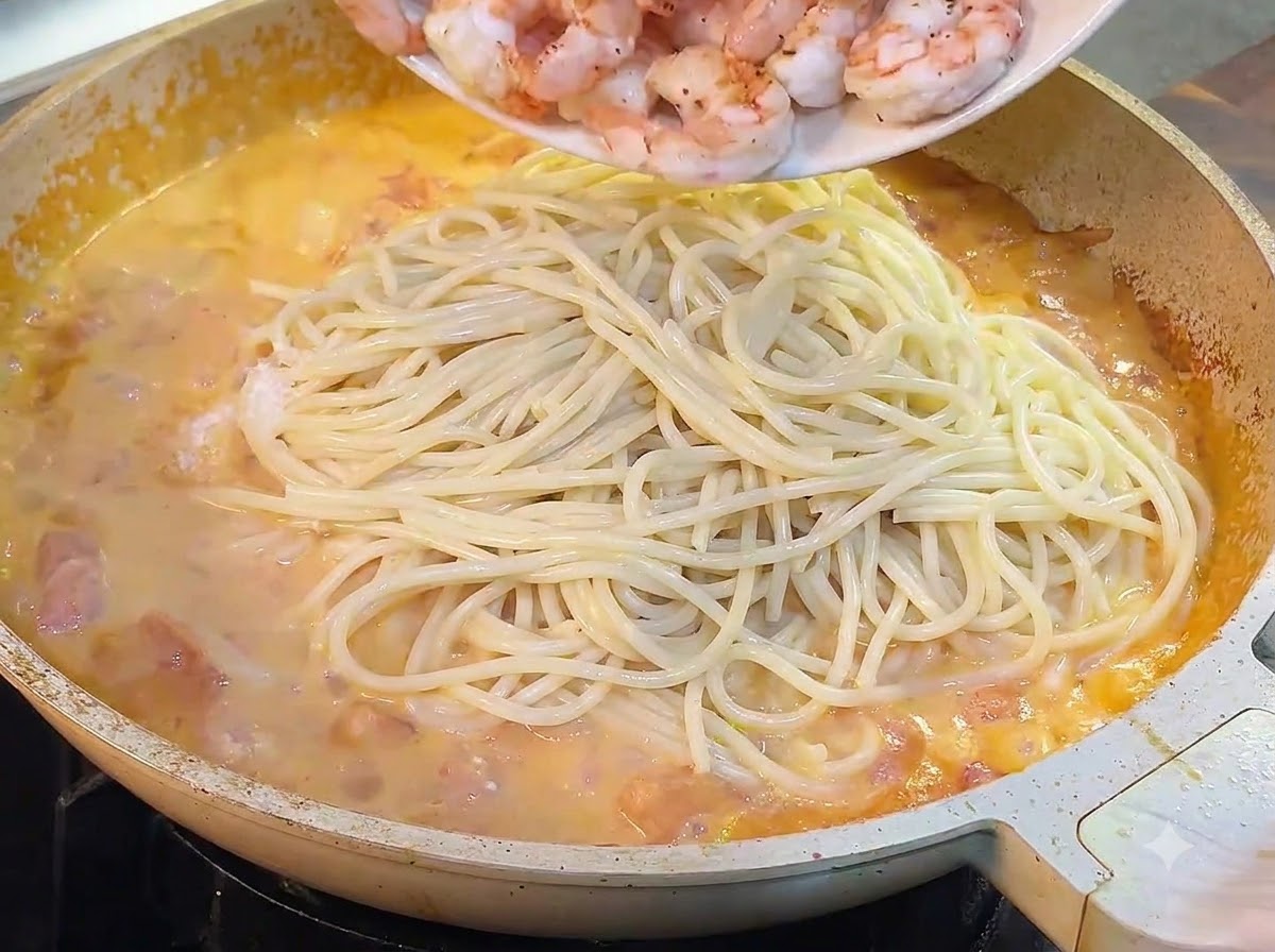 Usmażone krewetki zsuwane z talerza na patelnię ze spaghetti i sosem.