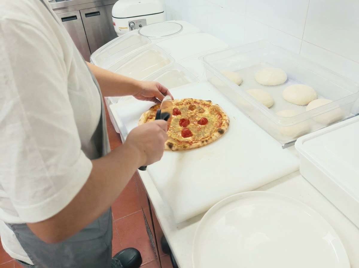Osoba używająca okrągłego noża do pizzy krojąca świeżo upieczoną pizzę na białej desce do krojenia.