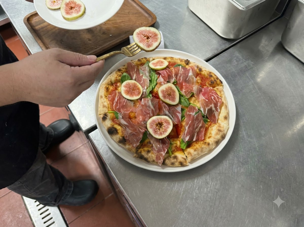 Plasterki świeżych fig i prosciutto układane widelcem na wierzchu upieczonej pizzy.