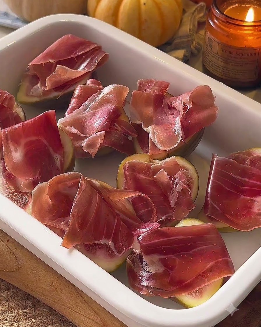 Zmontowane figi z prosciutto ułożone w białym naczyniu do zapiekania.