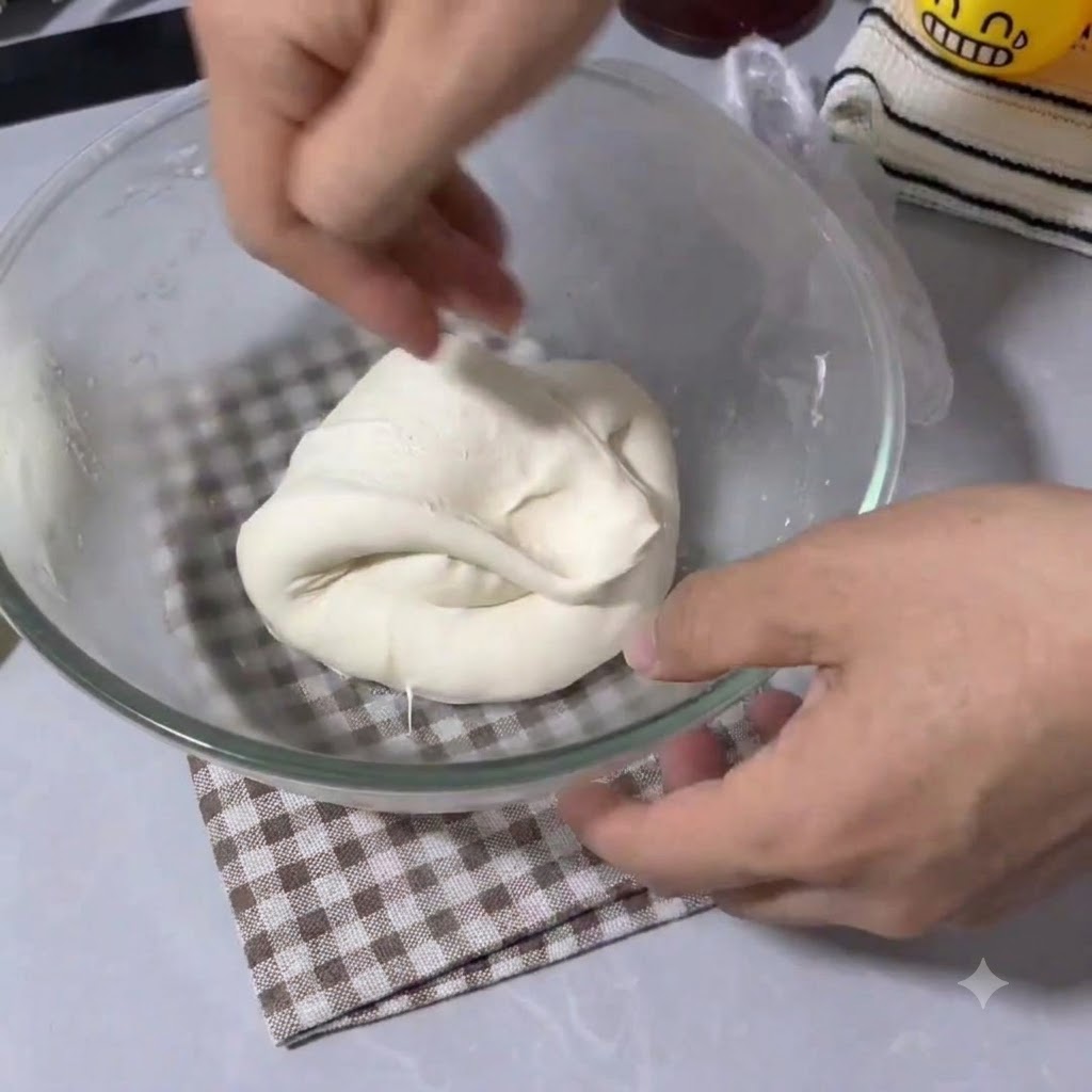 Dłonie składające i rozciągające elastyczne ciasto na pizzę w szklanej misce.