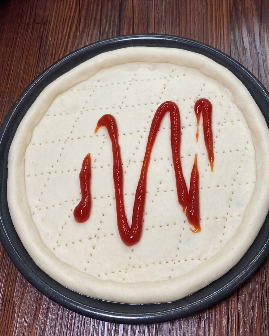 Starty ser mozzarella posypywany równomiernie na sos pomidorowy na cieście do pizzy.