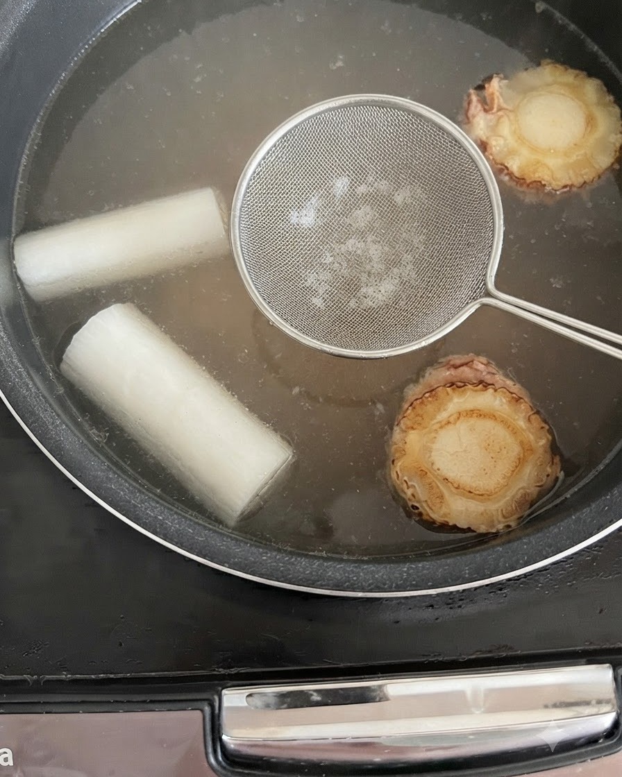 Łyżka cedzakowa nad gotującym się bulionem, służąca do zbierania piany.