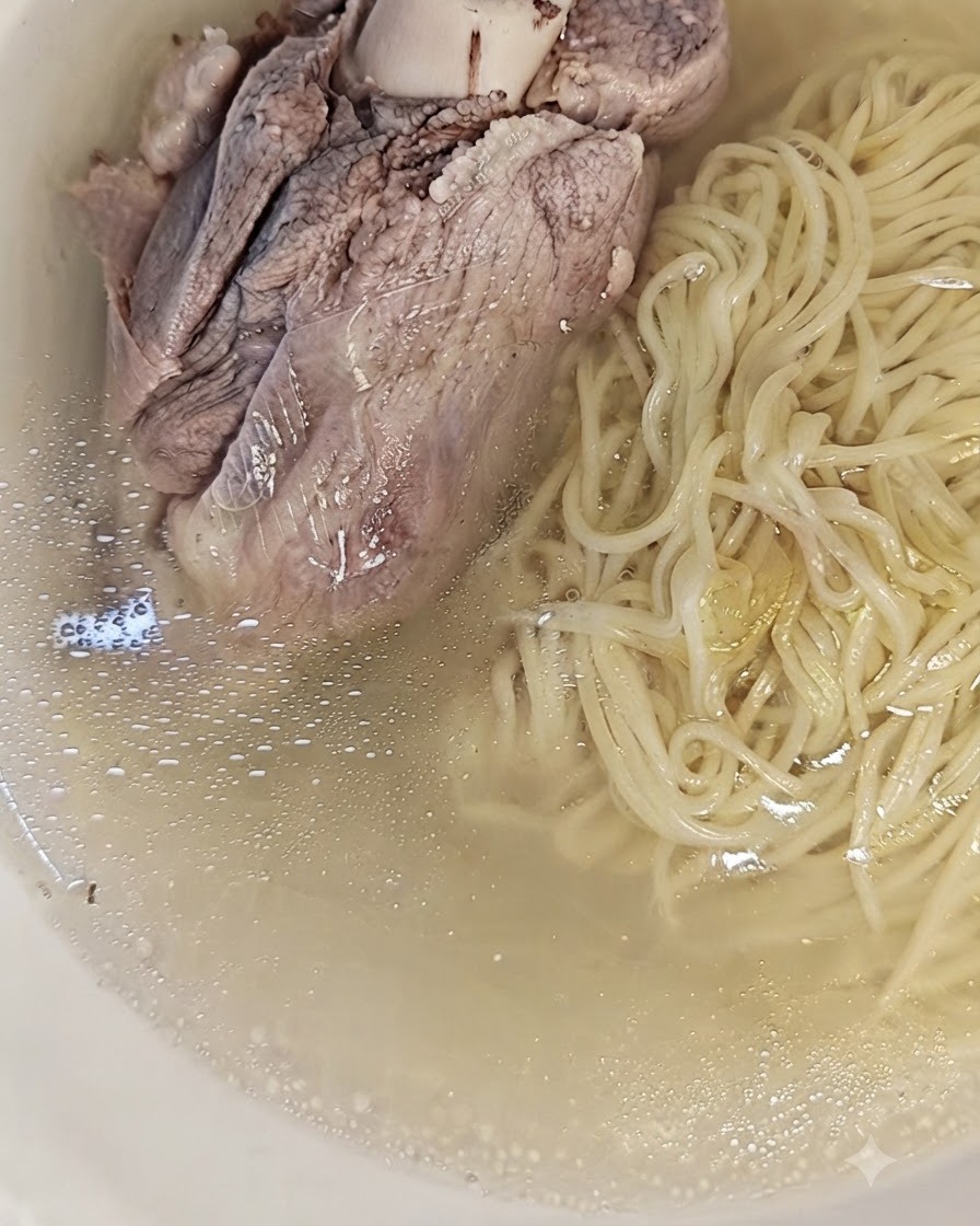Ugotowana kość wieprzowa z mięsem ułożona na makaronie w misce, gotowa do podania.