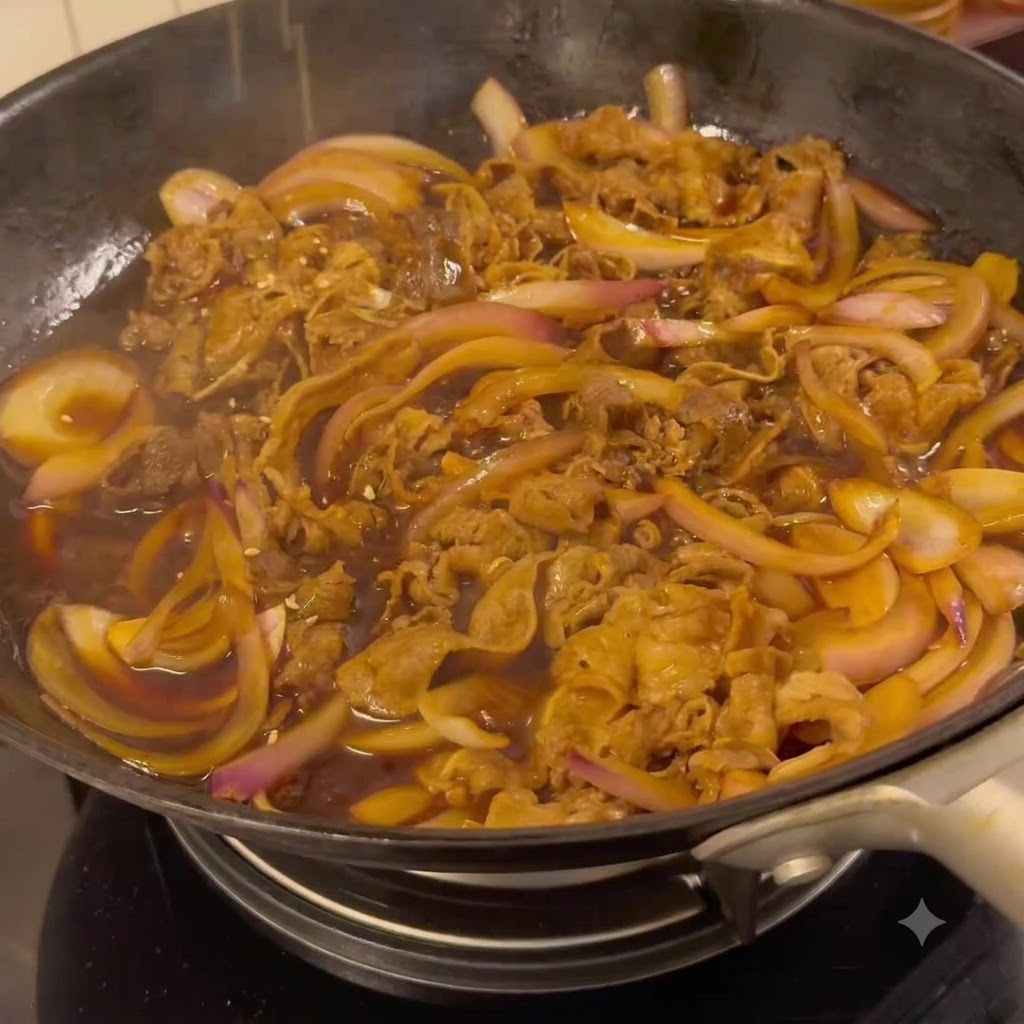 Wołowina i cebula duszące się w ciemnym, gęstym sosie teriyaki na patelni.