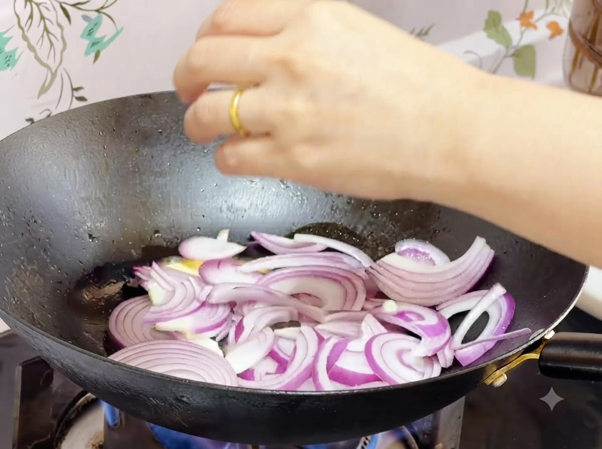 Pokrojona czerwona cebula smażąca się w roztopionym maśle w woku.