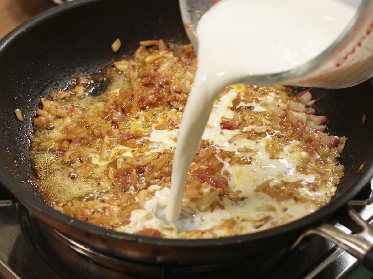 Mleko wlewane z kubka miarowego do patelni z duszącą się cebulą i curry.