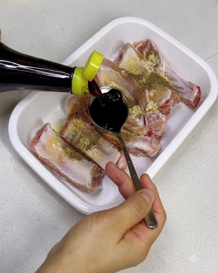 Nalewanie ciemnego sosu sojowego z butelki na surowe żeberka wieprzowe na białej tacy.