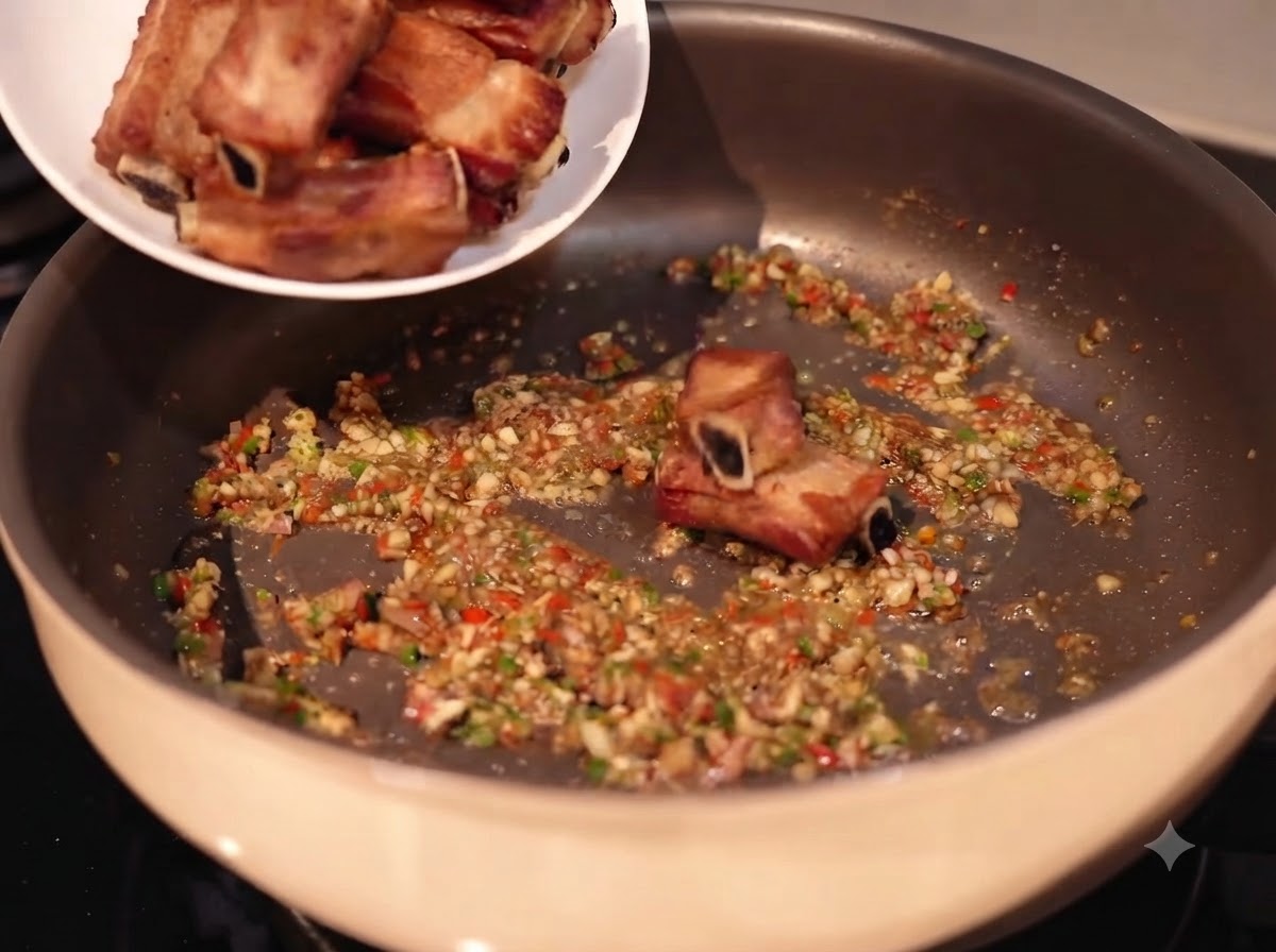 Żeberka wieprzowe dodawane z białego talerza na patelnię wypełnioną podsmażonym czosnkiem, chili i przyprawami.