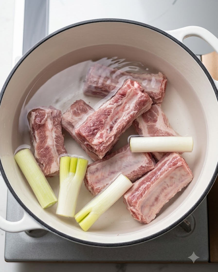 Świeże żeberka wieprzowe w garnku z zimną wodą, zieloną cebulką i aromatycznymi dodatkami przed zagotowaniem.