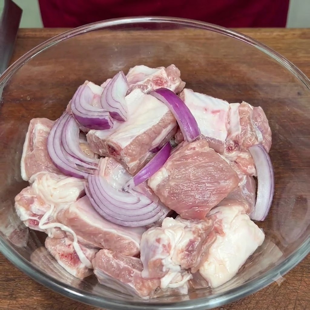 Pokrojona czerwona cebula i przyprawy dodane do surowych żeberek w szklanej misce.